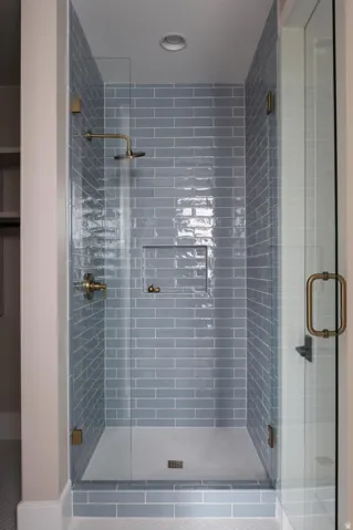 Walk-in shower with full glass enclosure, blue subway tile surround, recessed niche, and hexagonal mosaic tile flooring, accented by brass fixtures