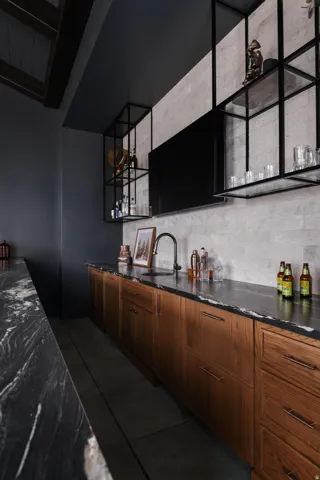 Wet bar featuring an integrated sink with a matte black faucet, wood-finish cabinetry, and dark stone countertops
