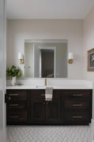 Bathroom vanity featuring a dark wood-finish cabinet with silver hardware, a white countertop, and an integrated rectangular sink with a gold-tone faucet