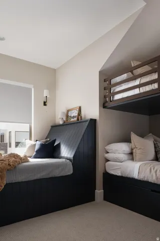 Built-in bed frames with integrated storage, neutral-toned carpeting, recessed ceiling lighting, and wall-mounted sconces