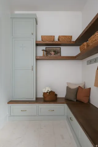 Built-in cabinetry with light blue-gray finish, wood-finish countertops, open wood-finish shelving, integrated storage drawers, and light-colored tile flooring