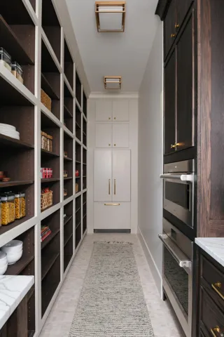 Expansive pantry featuring extensive built-in shelving, integrated refrigerator and freezer, built-in stainless steel double ovens, and recessed ceiling lighting