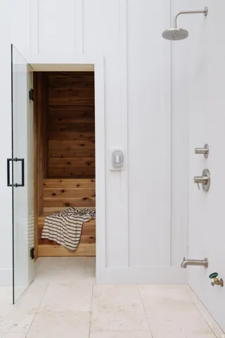 Integrated sauna with cedar interior and multi-tiered seating, featuring a clear glass door with matte black hardware