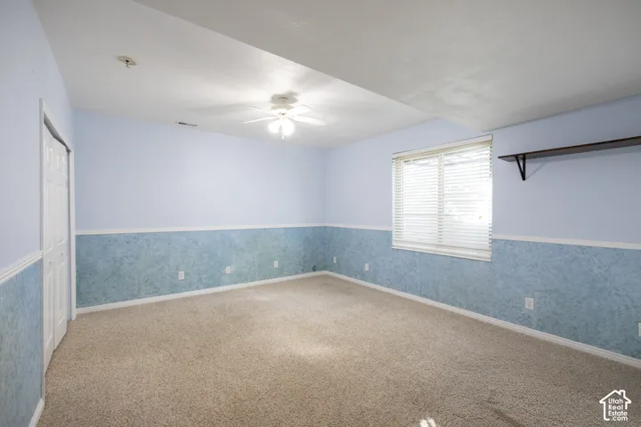 Carpeted room featuring a ceiling fan, a window with blinds, and a built-in wall shelf