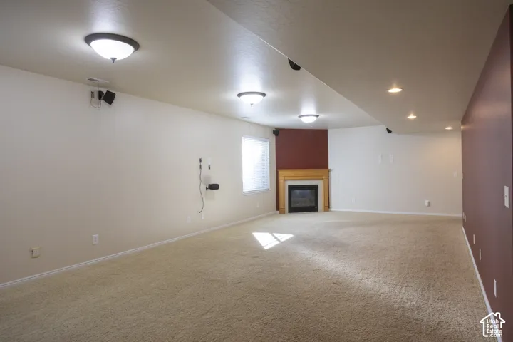 Expansive carpeted area featuring a corner fireplace with a wood-finish mantel, multiple ceiling-mounted light fixtures, and a window