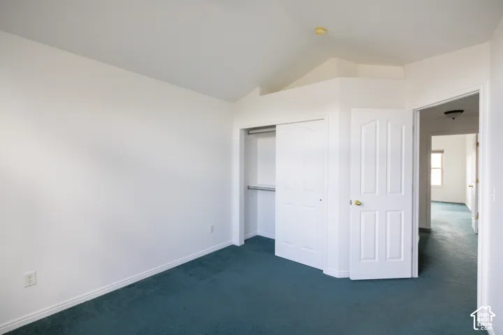 Vaulted ceiling, white walls, teal carpet, white paneled bifold closet doors, and a white paneled interior door