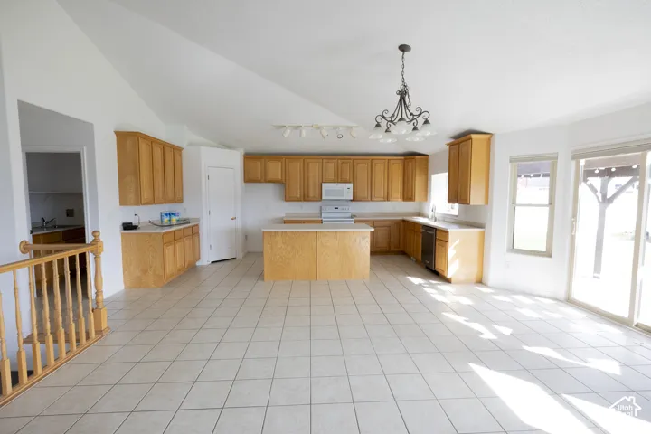Vaulted ceilings, a full kitchen with wood cabinetry and a central island, tile flooring, and a sliding glass door to the exterior