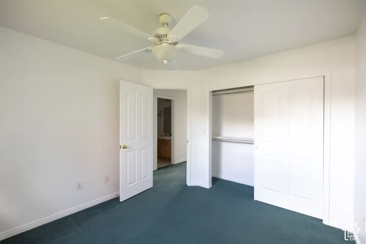 Ceiling fan with light fixture, carpeted flooring, white walls, bi-fold closet doors, and wood-finish vanity with counter in background