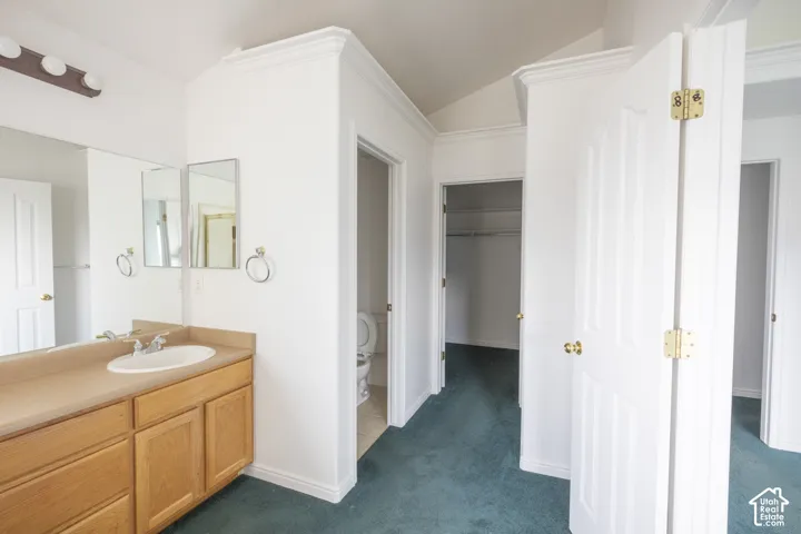 Master bathroom featuring dual vanities with wood cabinetry, a large walk-in closet with double doors and brass hardware, tile flooring in teal, and abundant natural light from multiple windows
