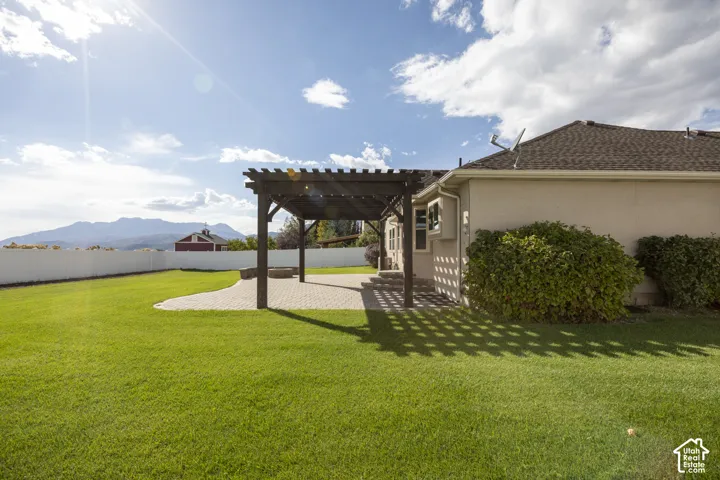 Expansive backyard featuring a pergola-covered paver patio, lush green lawn, and a white privacy fence