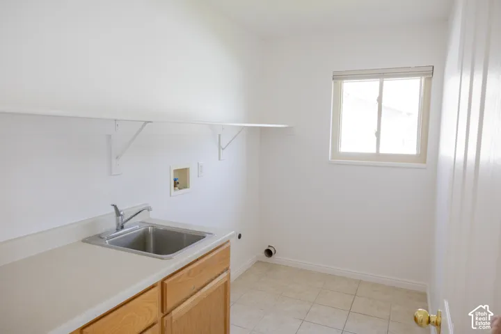 Utility room with light wood-finish cabinetry, a stainless steel sink, and a laminate countertop