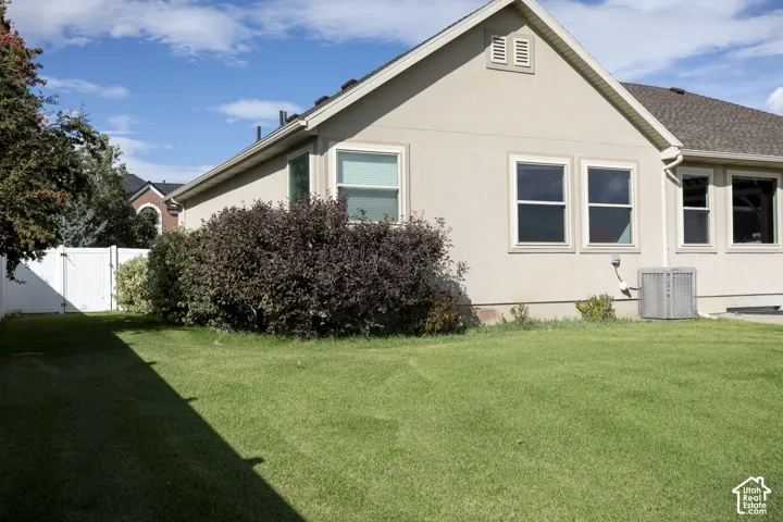 Expansive lawn area, stucco exterior, multiple windows, a white privacy fence, and mature landscaping