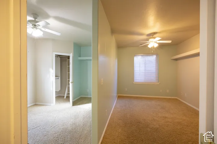 Spacious carpeted bedroom with ceiling fan, large window with blinds providing natural light, and generous floor plan