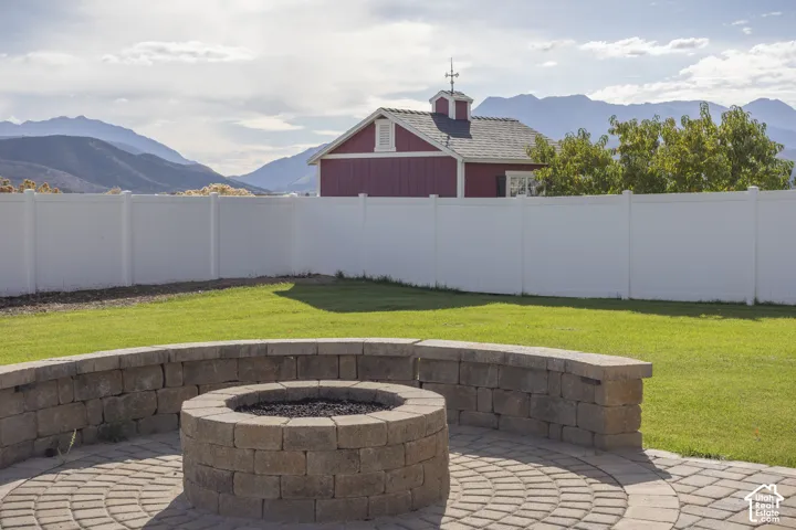 Expansive yard featuring a circular paver patio with a built-in fire pit, surrounded by a retaining wall with capstones, and a white privacy fence
