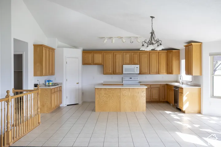 Open-concept kitchen featuring light-finish cabinetry, a central island, integrated appliances, and light-toned tile flooring
