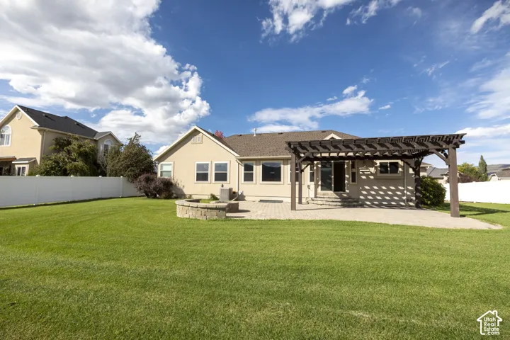 Expansive rear yard featuring a manicured lawn, full privacy fencing, and a stone-clad fire pit
