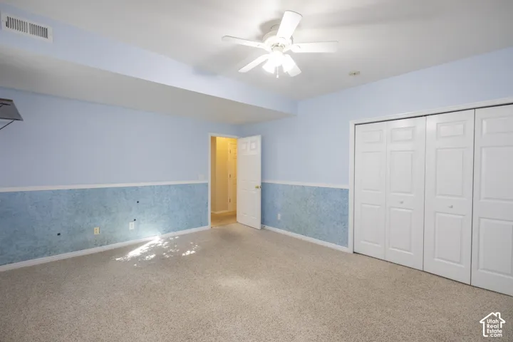 Spacious bedroom featuring soft blue and white two-tone wall treatment, neutral carpet flooring, ceiling fan with integrated lighting, and double closet storage with white six-panel doors