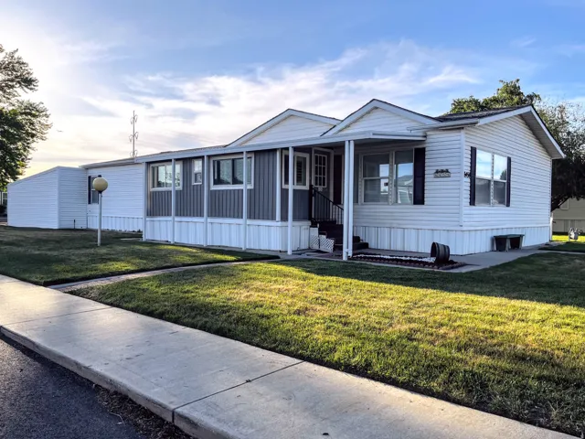 White siding exterior with a contrasting gray accent panel, a covered front entry, landscaped lawn, and a sidewalk border