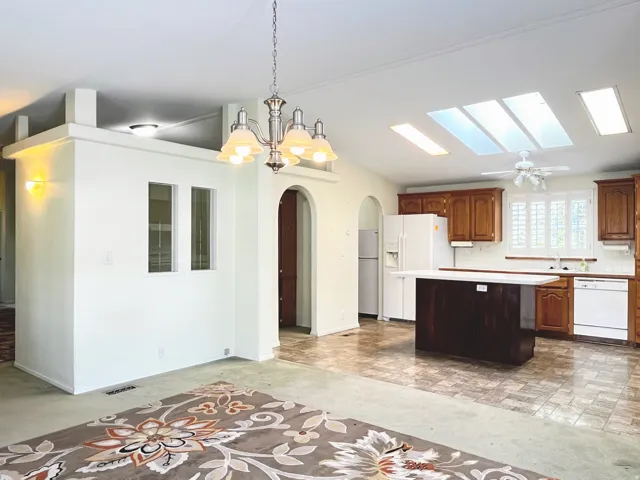Kitchen and living area featuring a vaulted ceiling with skylights, white walls, and an arched doorway