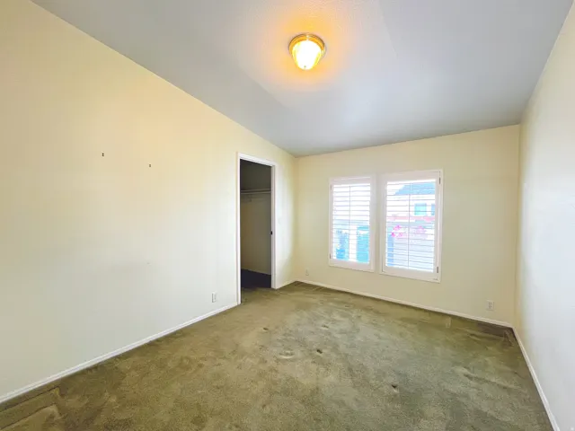 Room featuring wall-to-wall carpeting, dual windows with plantation shutters, a ceiling-mounted light fixture, and an open doorway revealing a closet