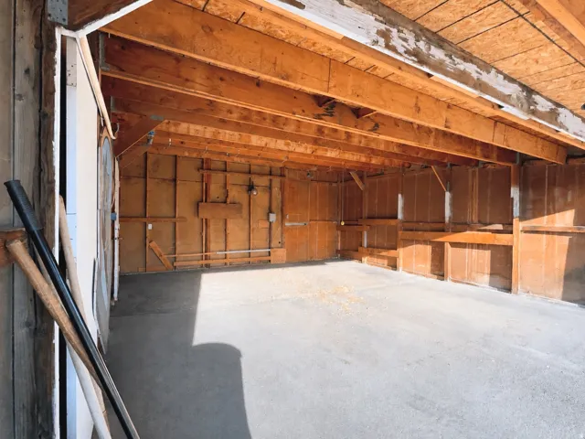 Spacious garage interior featuring exposed wood beam ceiling, concrete flooring, wood paneled walls, and built-in shelving