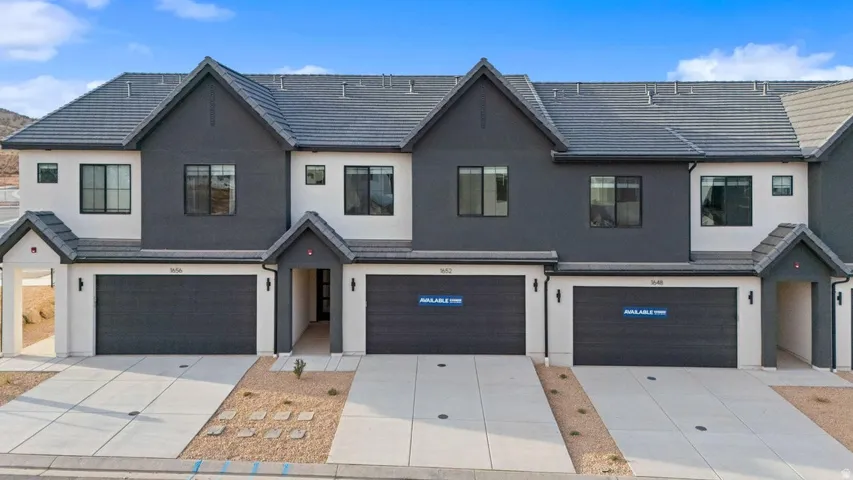 Contemporary townhome-style exterior featuring a multi-tone facade, dark roof, black-framed windows, attached garages with dark doors, and integrated covered entrances