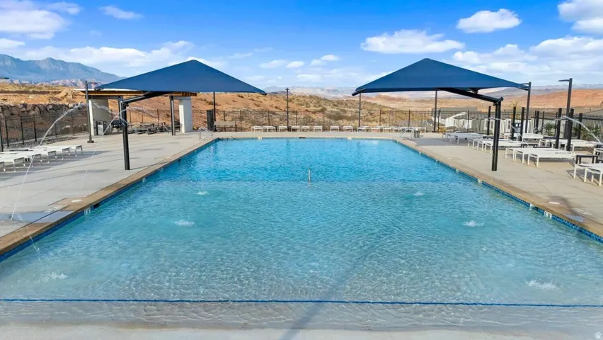 Expansive community pool featuring a large swimming area, integrated water features, concrete decking, and two shade structures