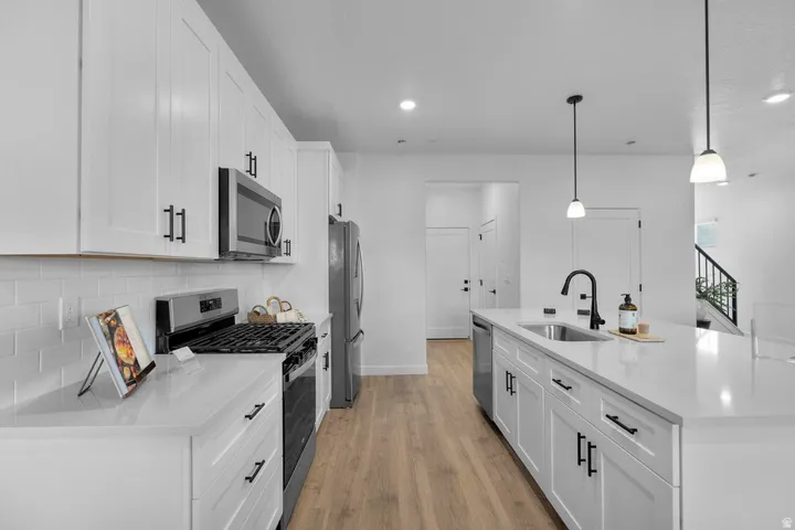 Contemporary kitchen featuring white shaker cabinetry, stainless steel appliances, light-toned countertops, and wood-finish flooring