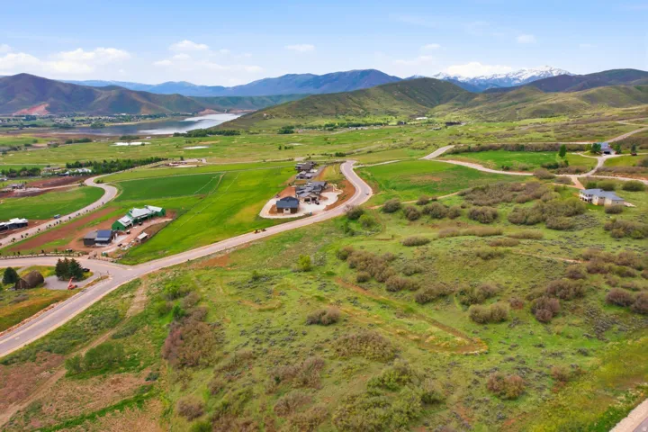 Expansive green landscape with distant mountains featuring snow-capped peaks, a prominent body of water, and residential structures