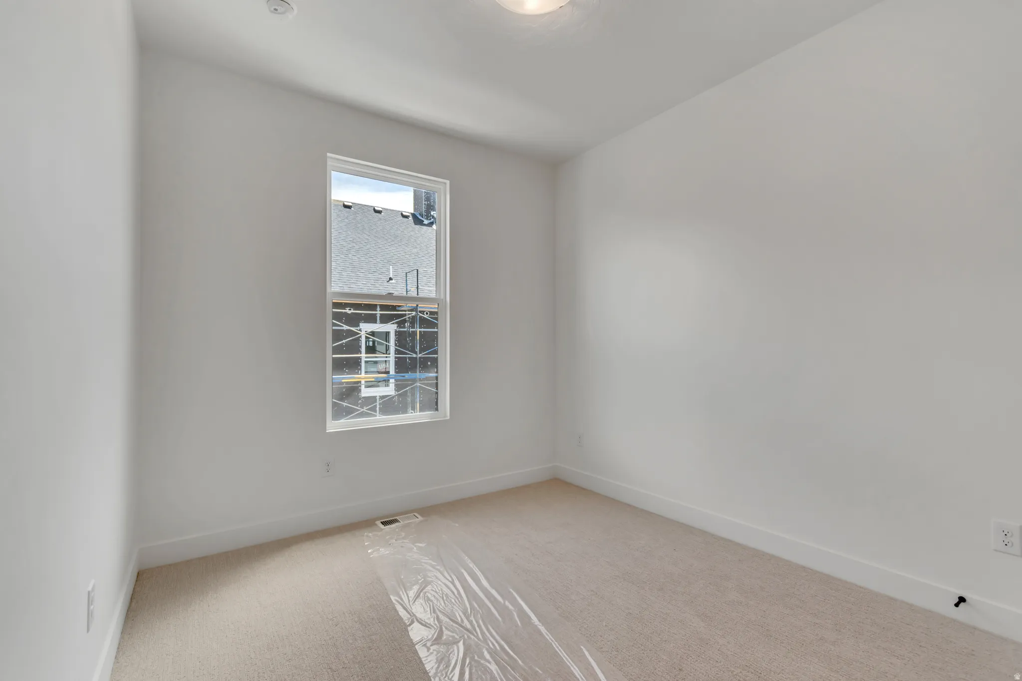Light-filled interior space featuring a single window, white wall finishes, and neutral-toned carpeting
