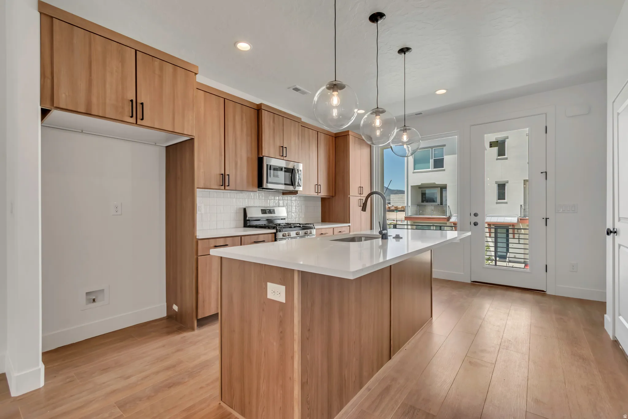 Kitchen featuring wood-finish cabinetry, white subway tile backsplash, and a central island with a sink