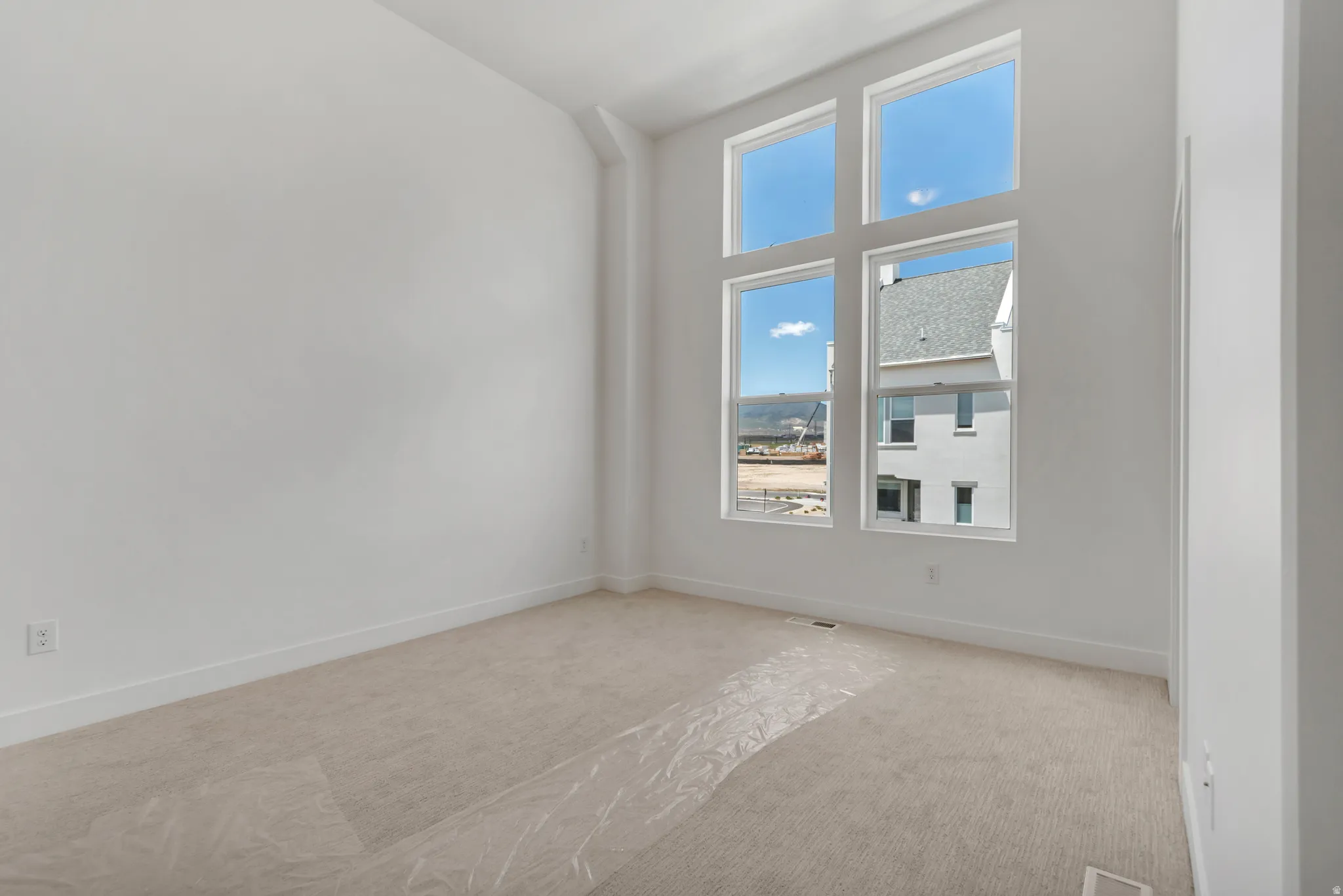 Spacious room featuring a towering window array, white walls, light-colored carpet, and white baseboards