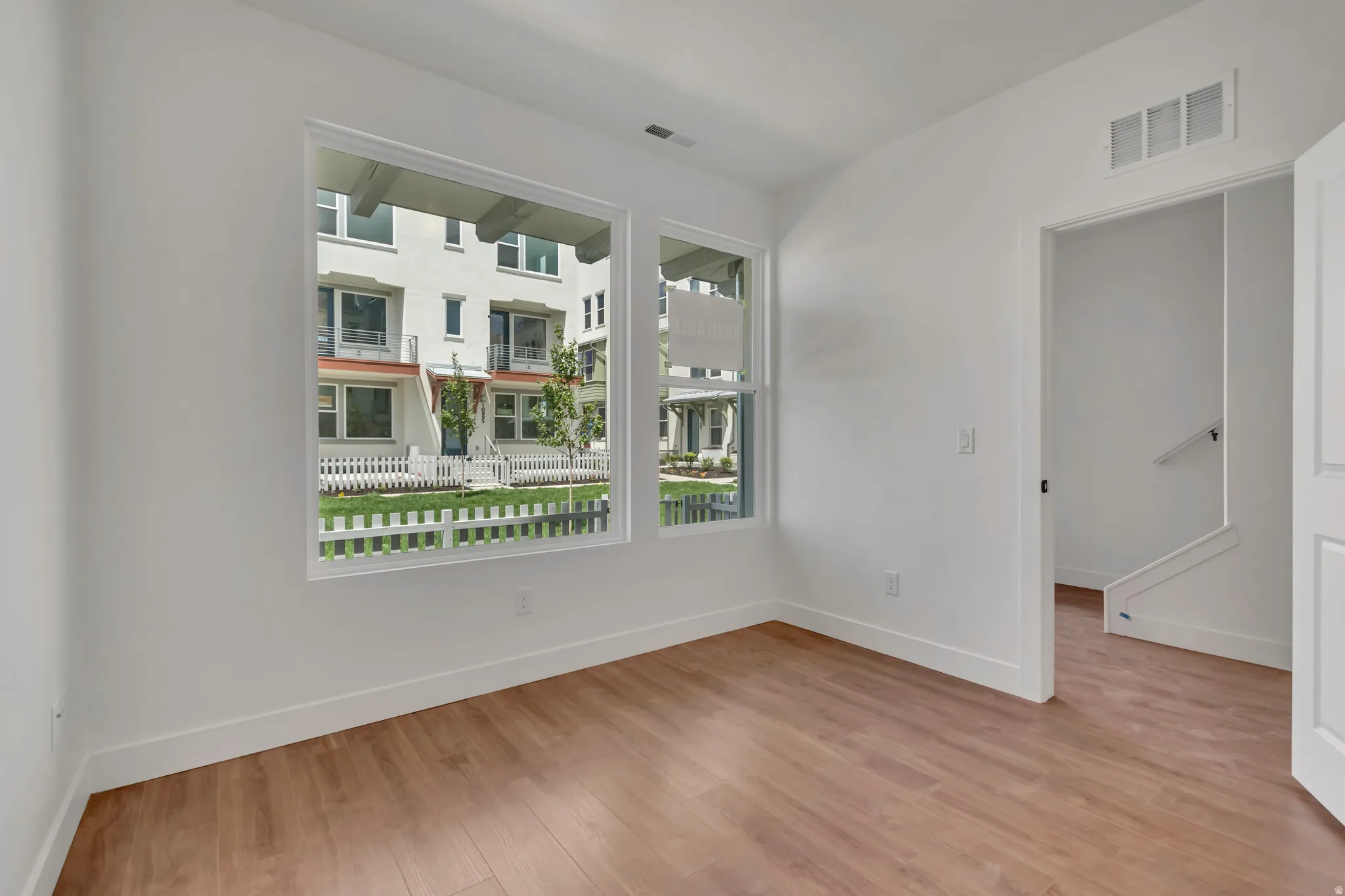 Room with wood-finish flooring, crisp white walls, and a large window offering exterior views
