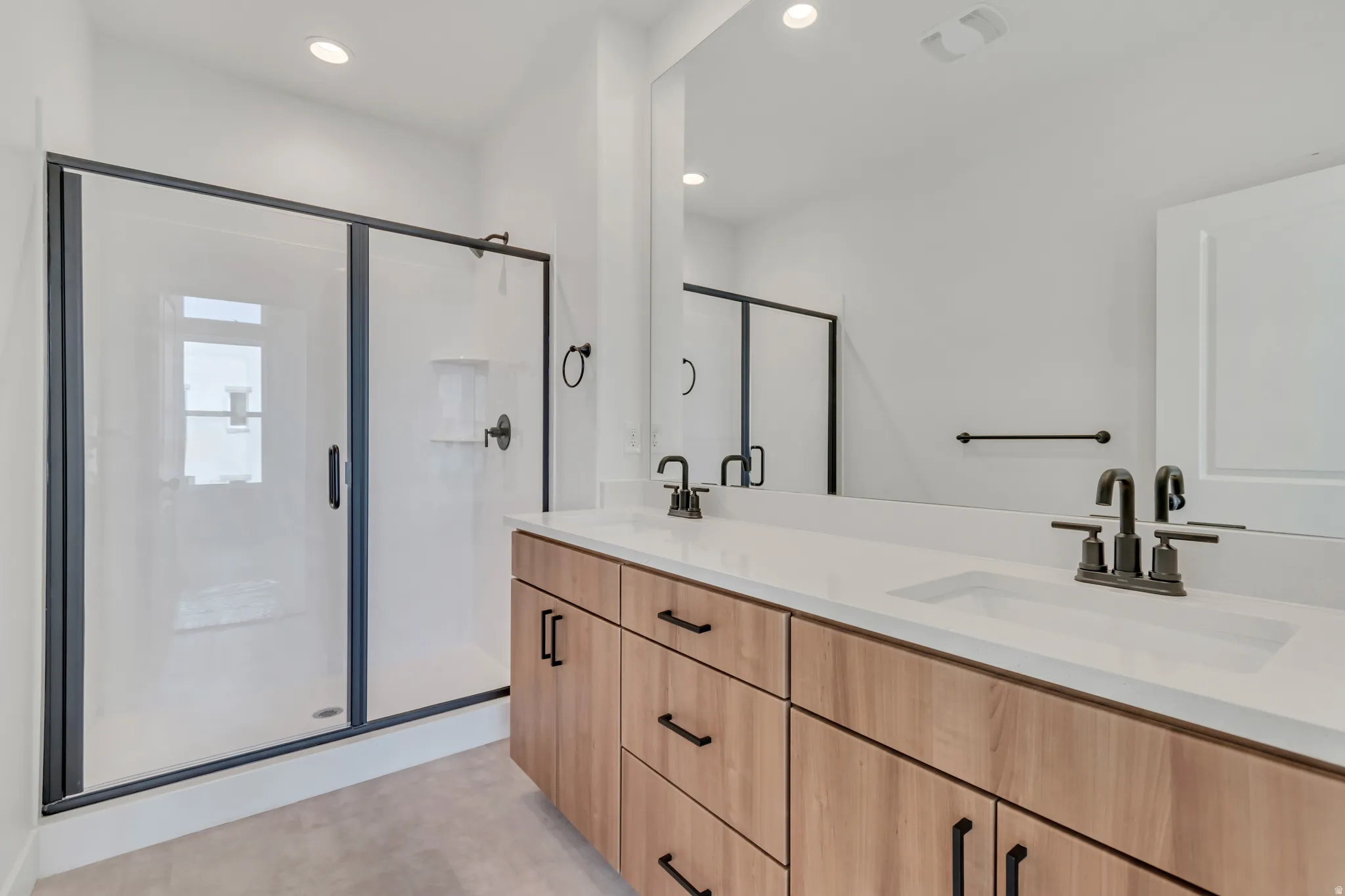 Modern bathroom featuring a double vanity with light wood-finish cabinetry, white countertops, and matte black fixtures