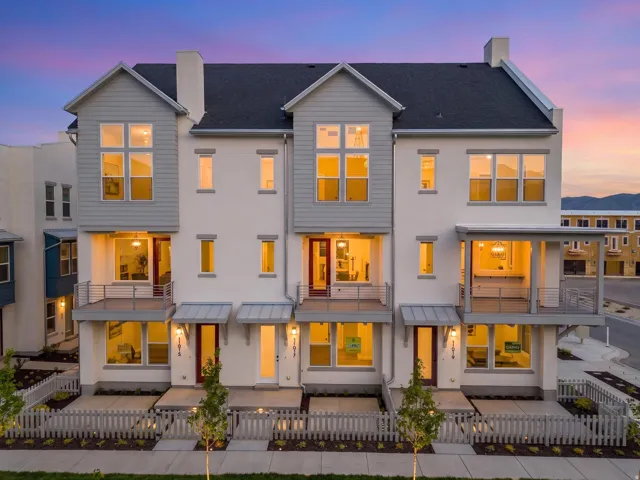 Modern townhome exterior featuring white stucco, gray siding, multiple balconies with metal railings, and individual fenced front yards