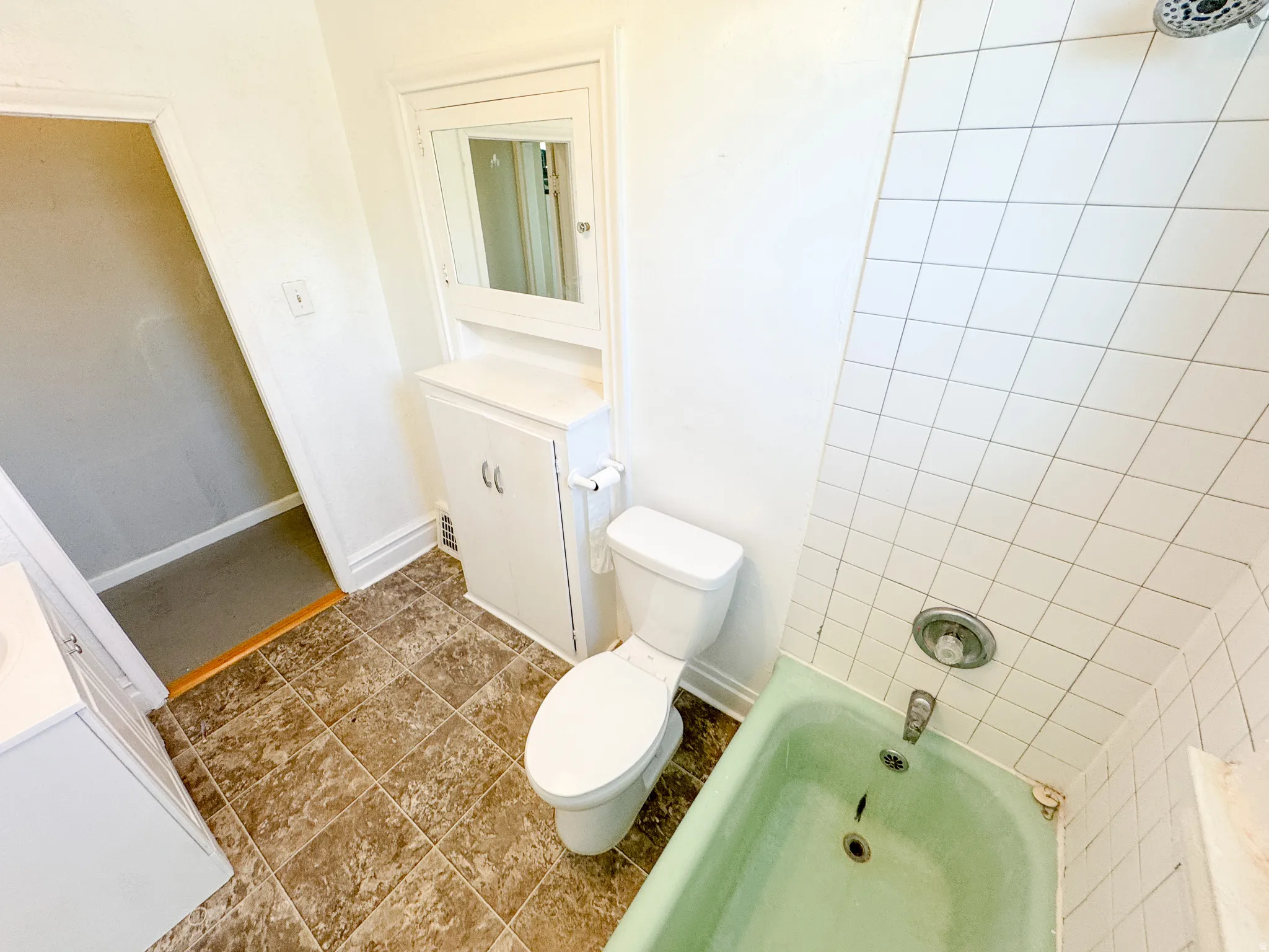 Bathroom featuring a green bathtub, white tile surround, and a built-in medicine cabinet with lower cabinetry