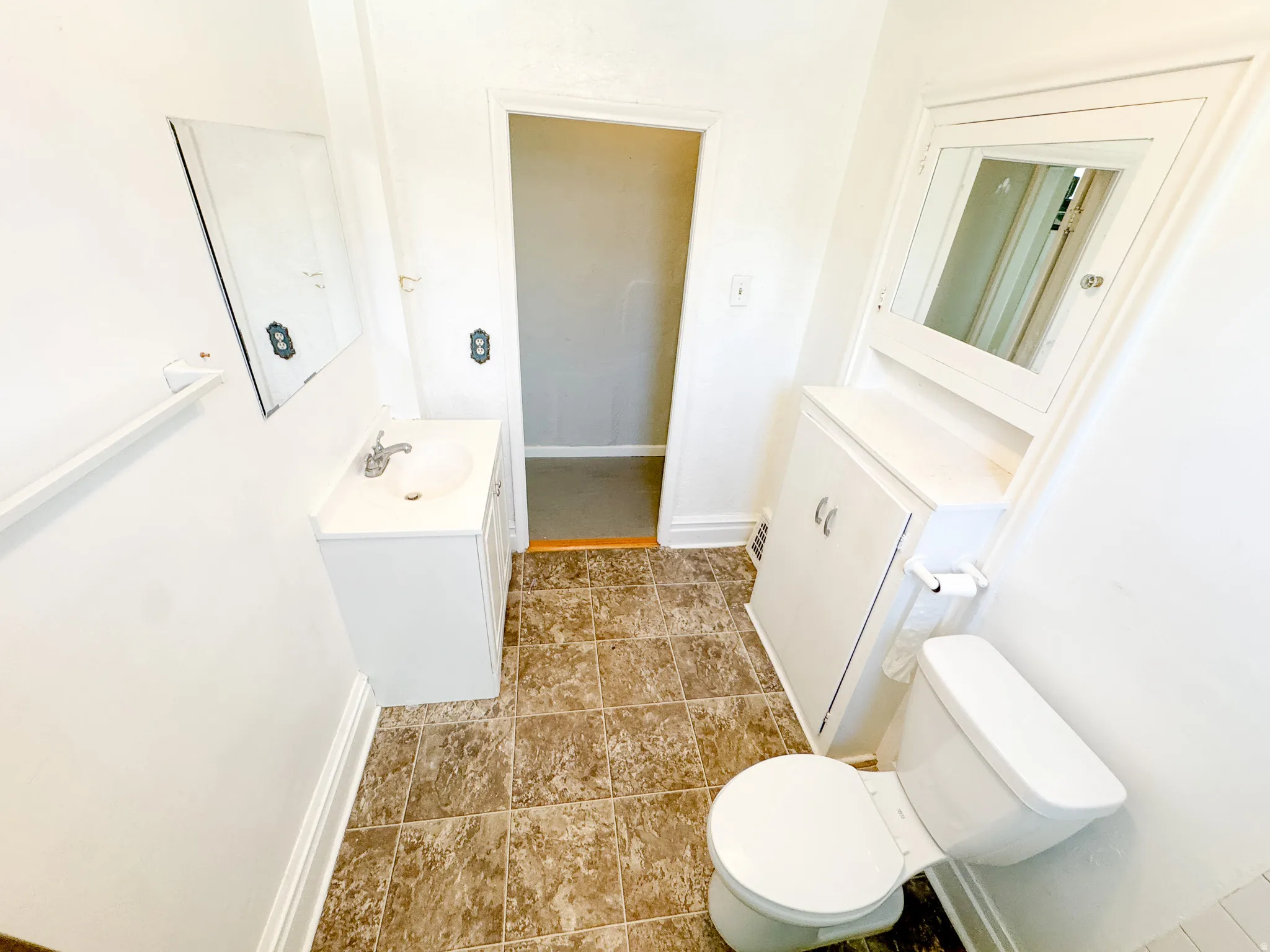 Bathroom featuring a white vanity with integrated sink, chrome faucet, wall-mounted mirror, white toilet, and built-in storage cabinet with a mirrored medicine cabinet