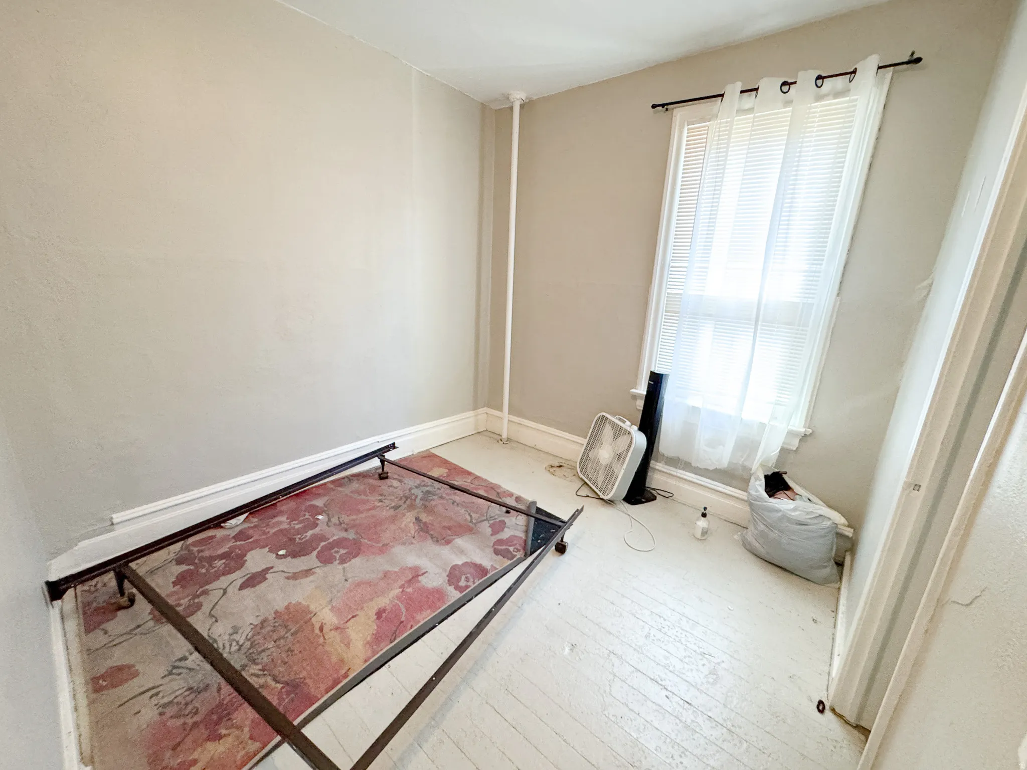 Room featuring a single window with white blinds and sheer curtains