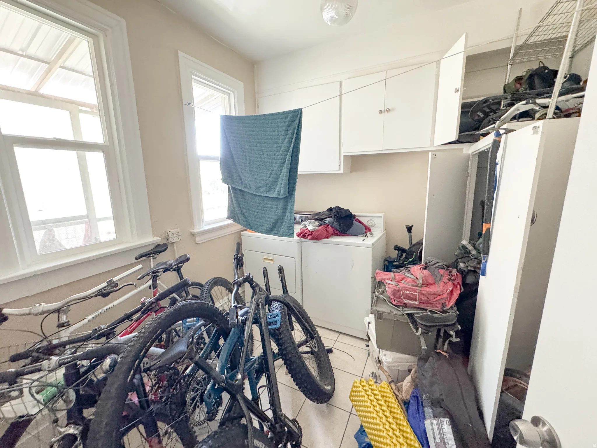 Utility room featuring white shaker cabinetry, two double-hung windows, a washer, and tile flooring