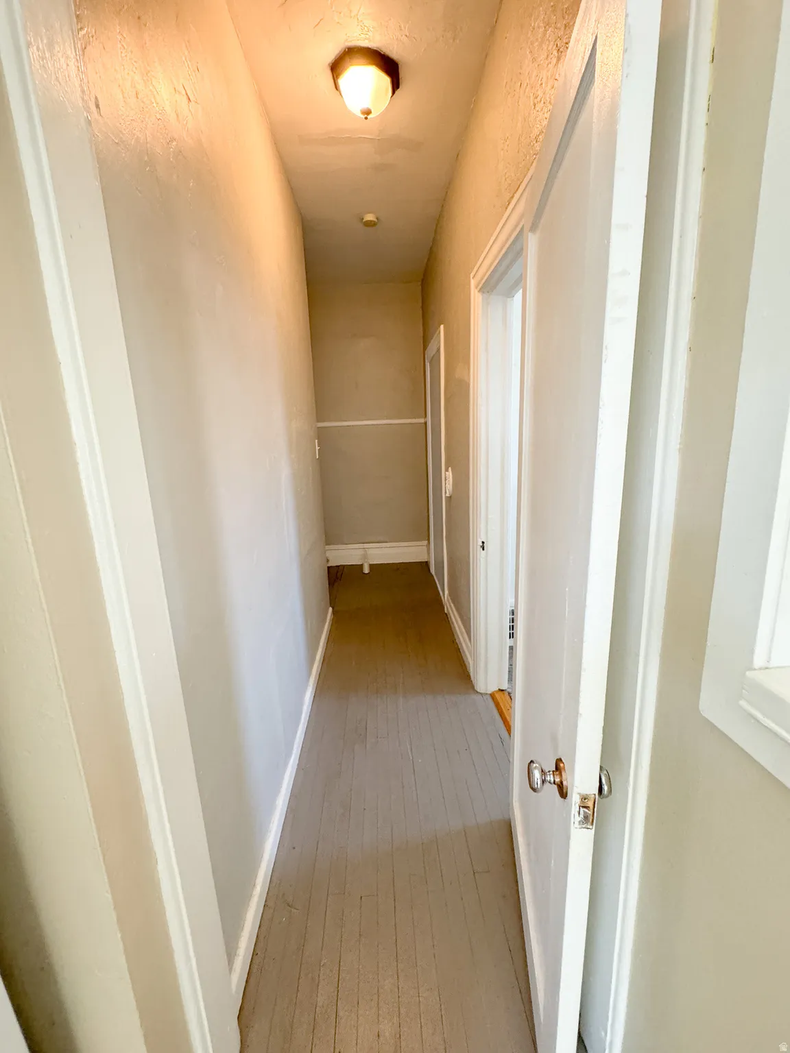 Hallway featuring wood-finish flooring, white trim, and a ceiling-mounted light fixture
