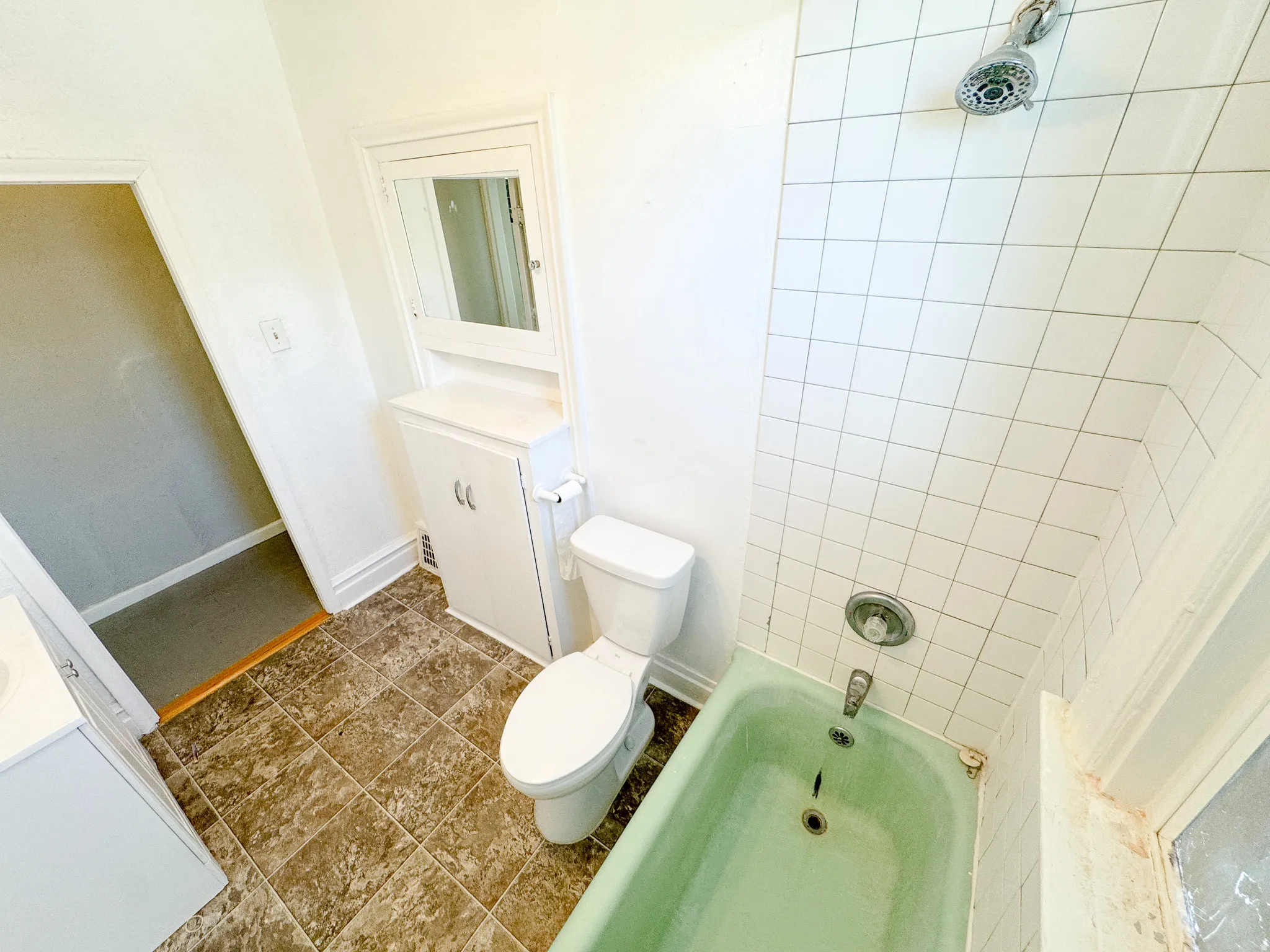 Bathroom featuring a green bathtub with a shower fixture, white tile surround, and a white toilet