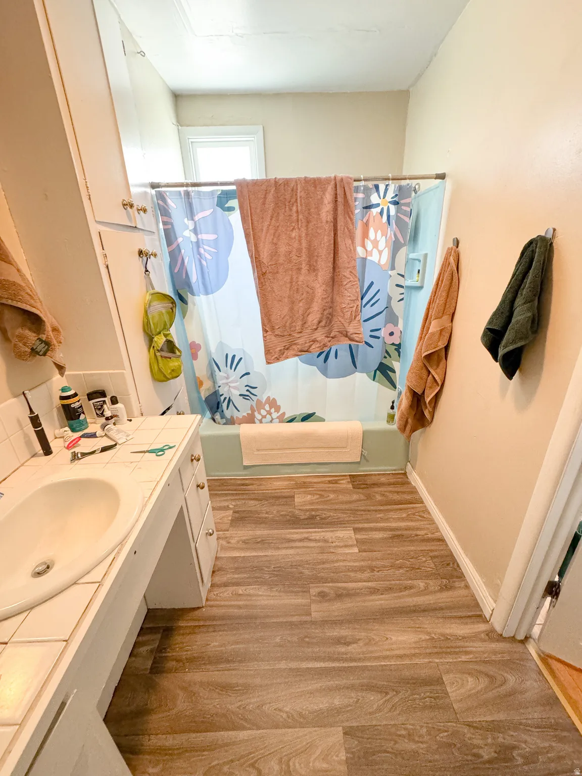 Bathroom featuring wood-finish flooring, a built-in vanity with a white countertop and integrated sink, and an alcove bathtub