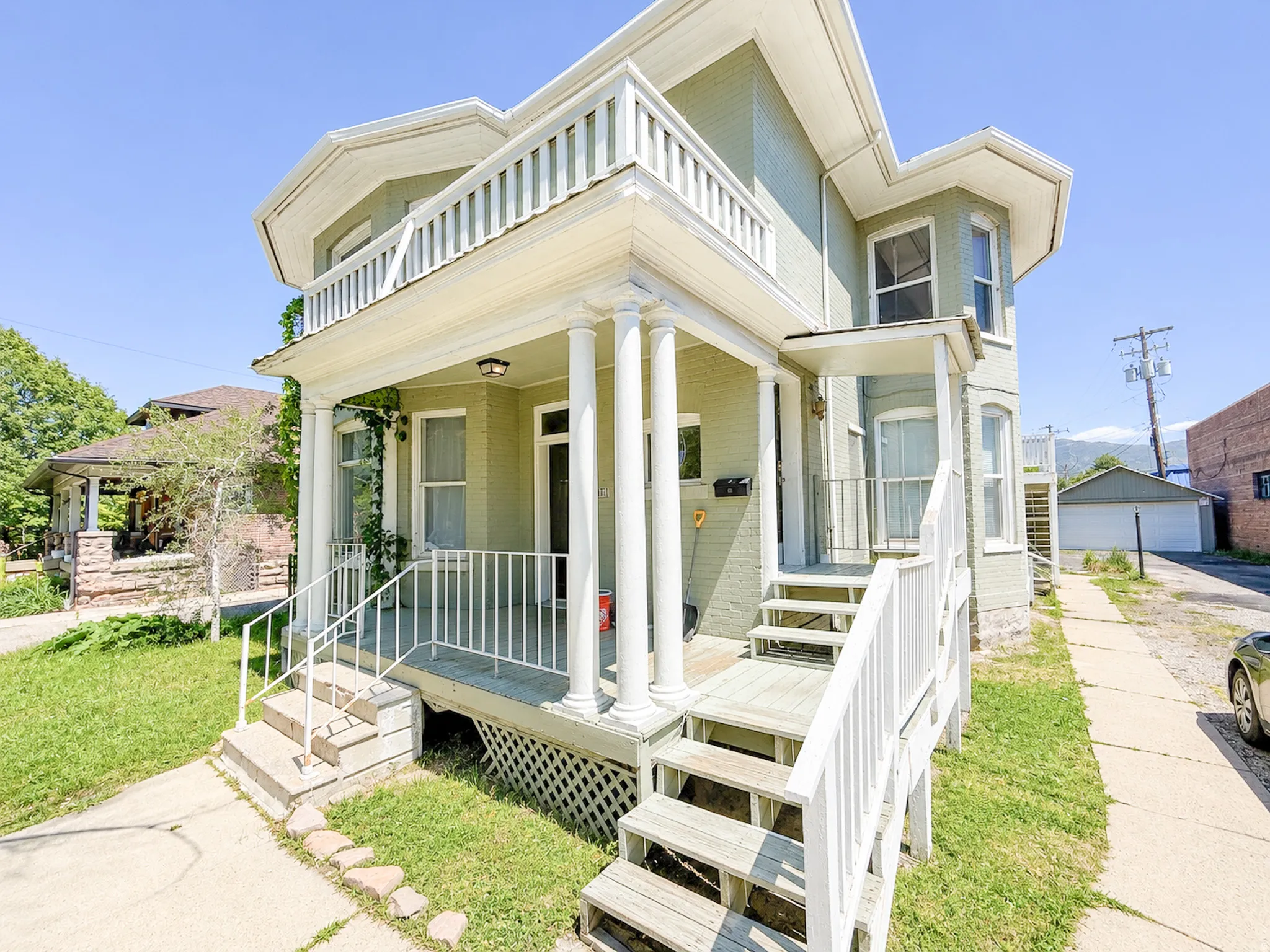 Exterior facade featuring a covered porch with white columns, a second-story balcony, multiple windows, and a side entrance with stairs