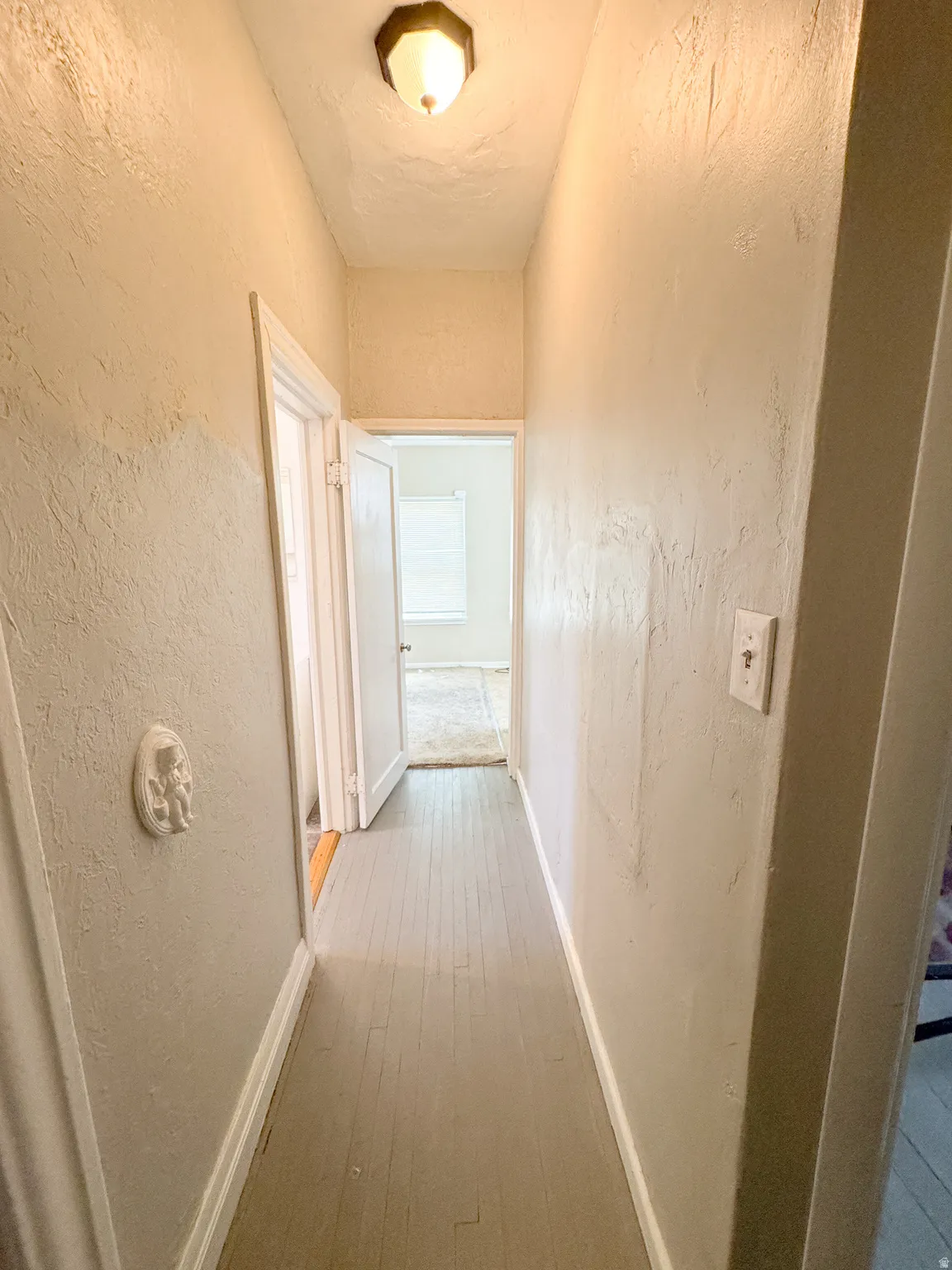 Hallway featuring wood-finish flooring, textured walls, and a ceiling-mounted light fixture