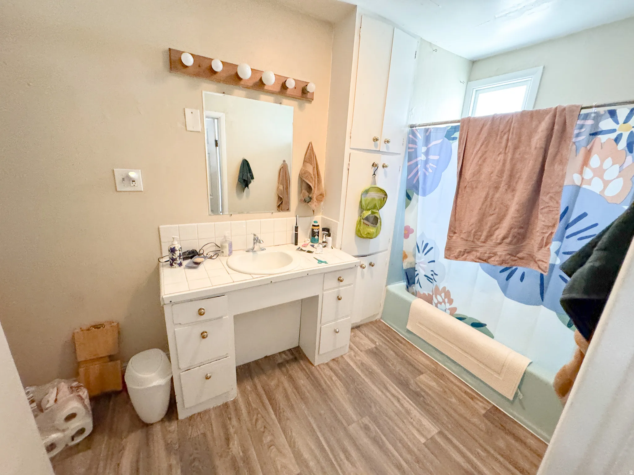 Bathroom vanity with integrated sink, white tile backsplash, and wood-finish flooring