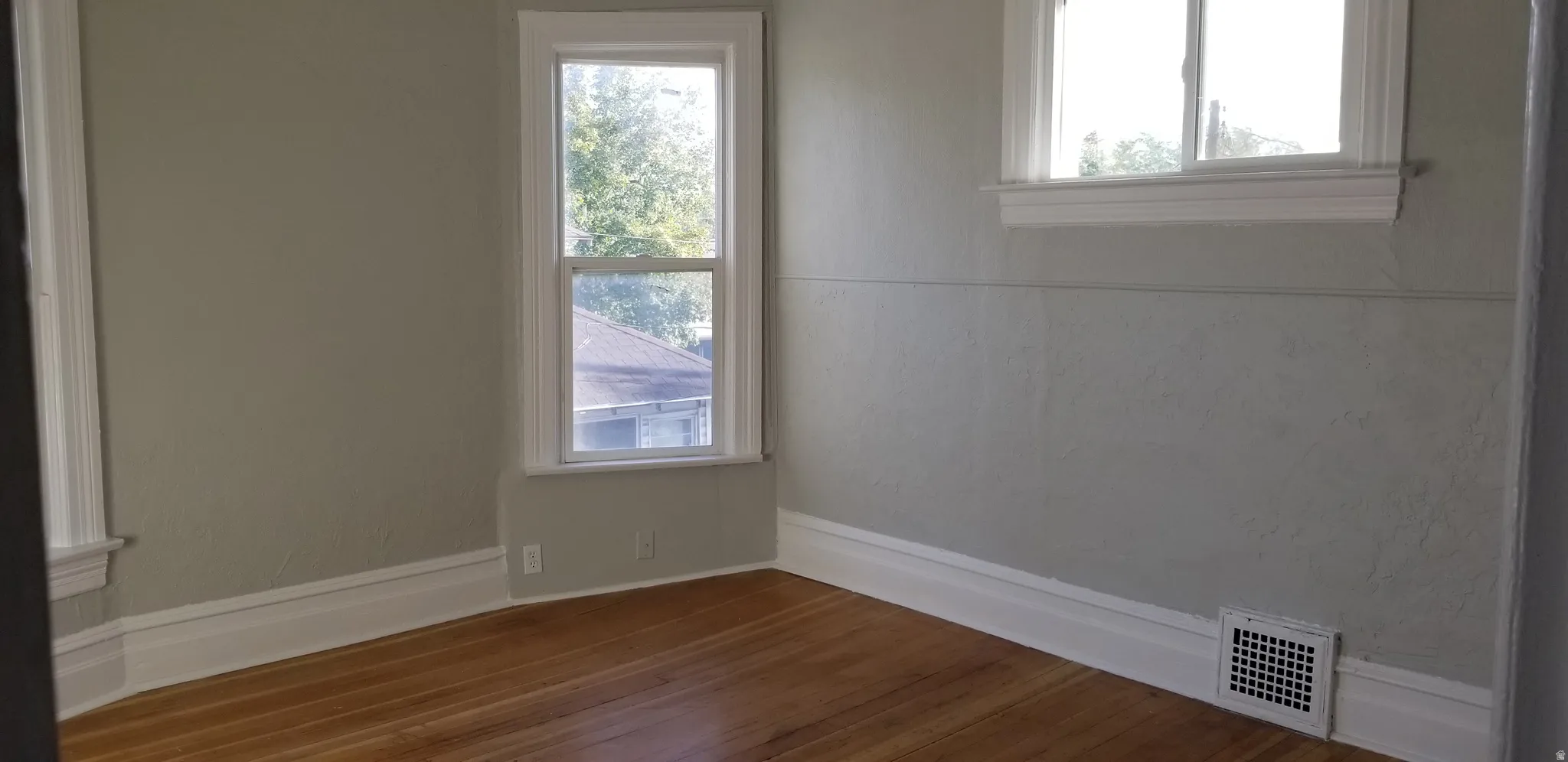 Interior space featuring wood-finish flooring, light-toned walls, two windows with white trim, and white baseboards