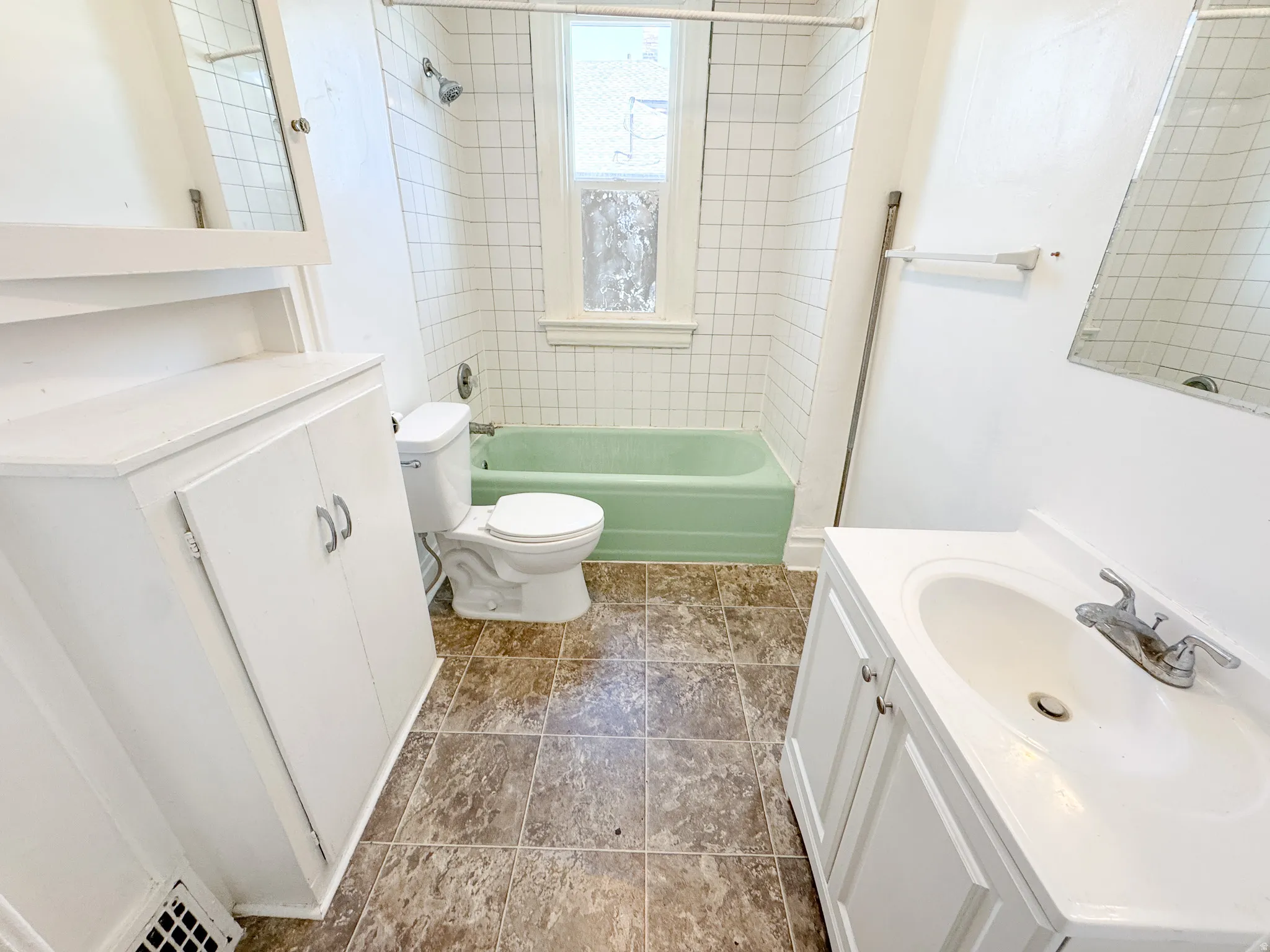 Bathroom featuring a green bathtub, white subway tile shower surround, and a white vanity with integrated sink