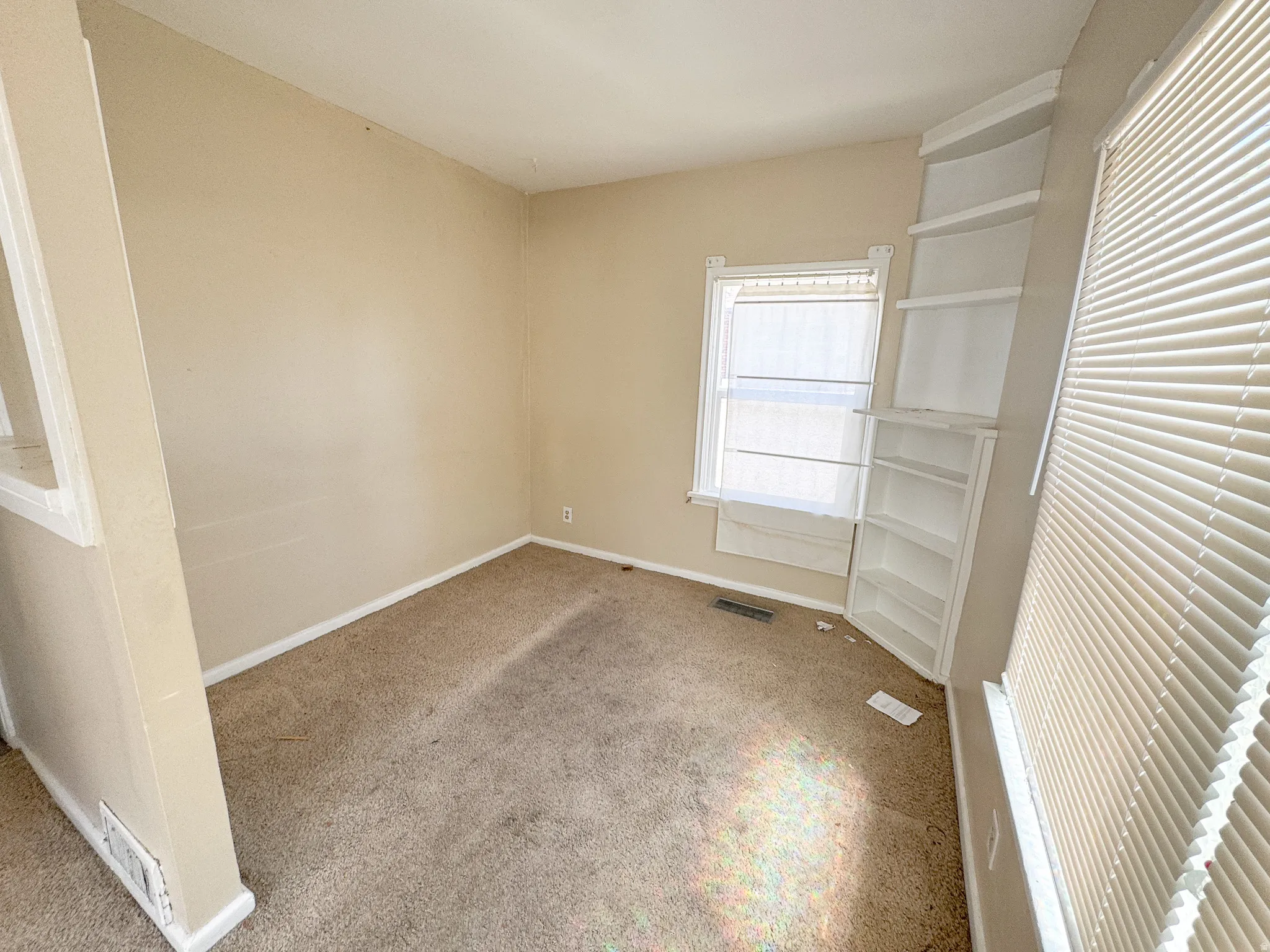 Corner room featuring built-in shelving, a window with horizontal blinds, and neutral-toned carpet