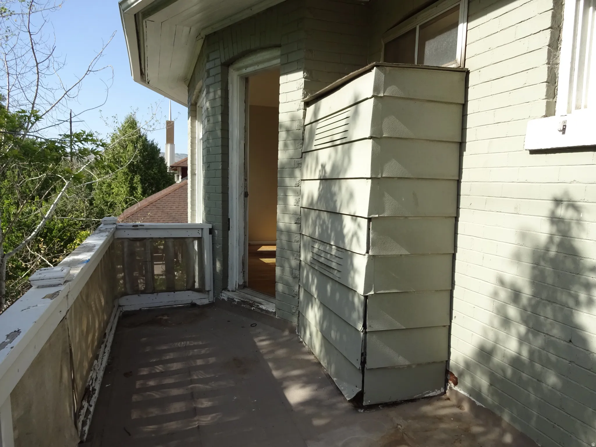 Balcony with painted wood railing, brick exterior, and open doorway