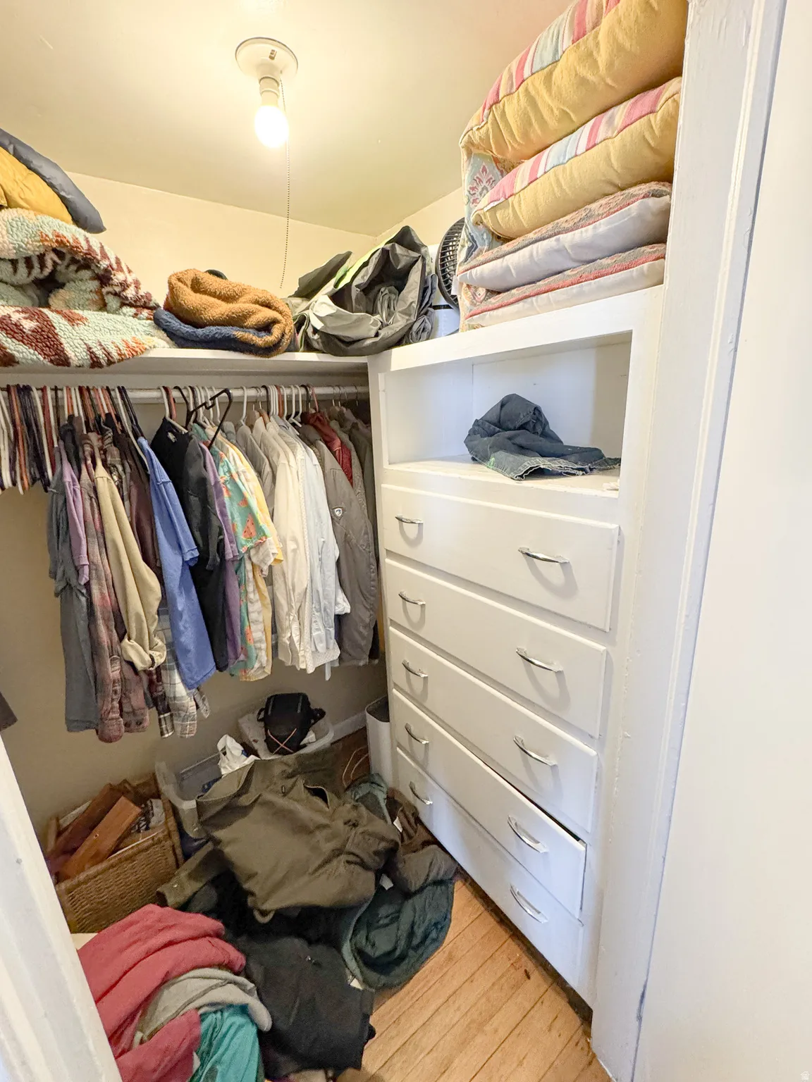 Walk-in closet featuring wood-finish flooring, built-in shelving, and a built-in dresser with chrome hardware